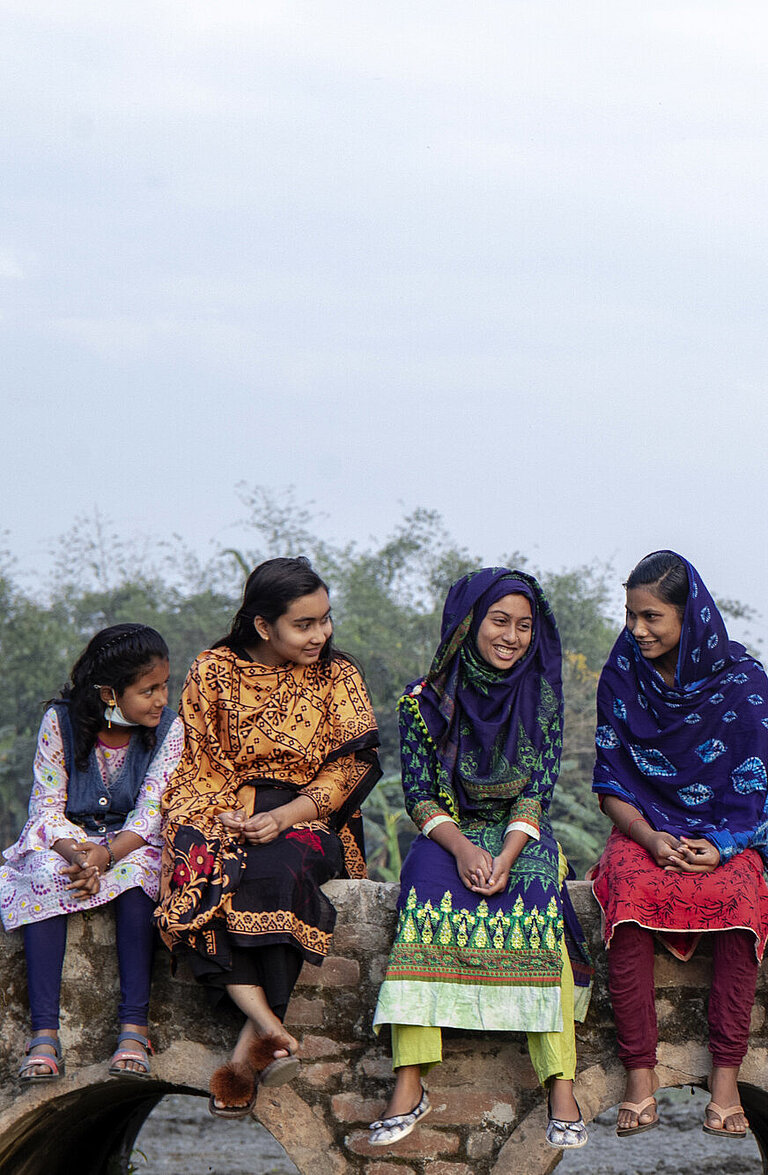 Mädchen in Bangladesch sitzen auf einer Brücke und unterhalten sich.