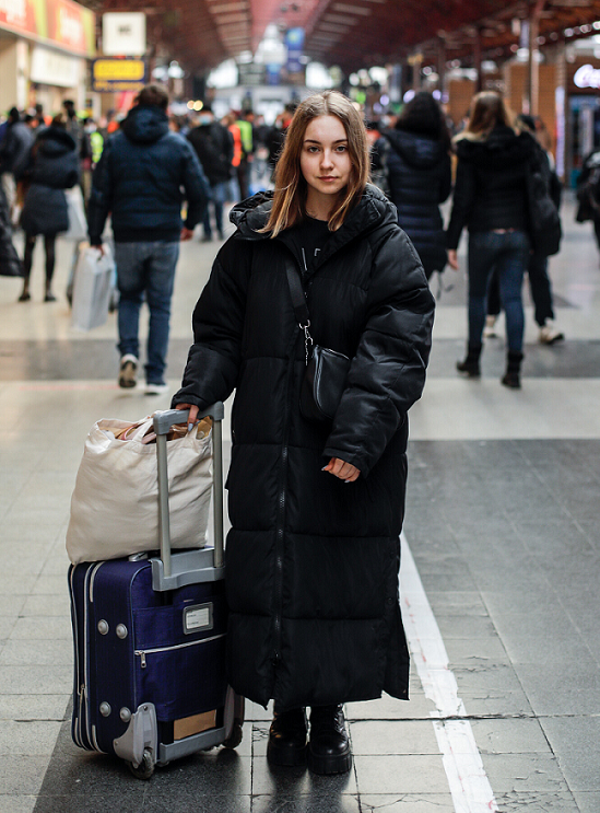 Eine junge Frau steht mit einem Koffer und einem Beutel im Bahnhof