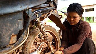 Eine junge Frau hockt vor einem Motorrad und zieht eine Schraube nach.