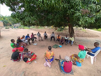 Menschen sitzen im Kreis unter einem Baum und sprechen miteinander