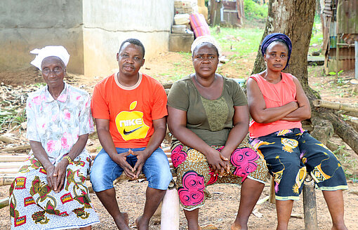 Vier Menschen sitzen nebeneinander auf einer Bank vor einem Baum