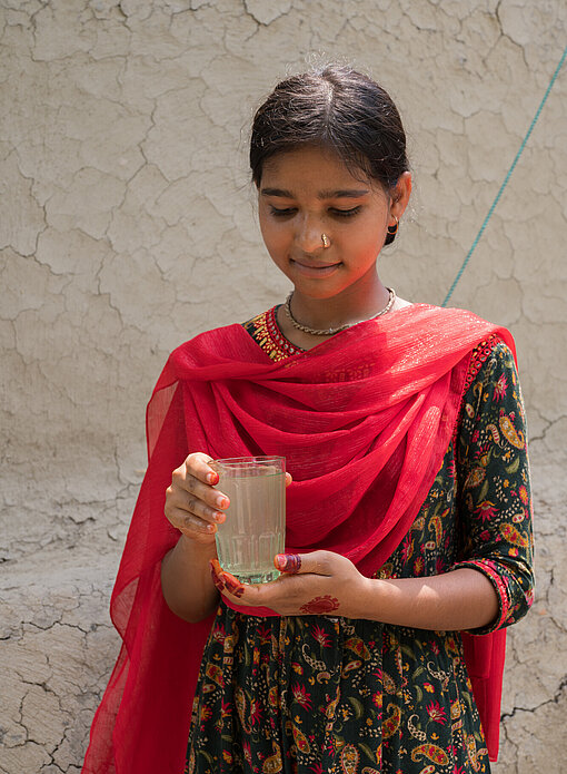 ein Mädchen aus Bangladesch hält ein Glas ungefiltertes Wasser in der Hand