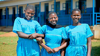 Drei Schülerinnen in blauen Schuluniformen stehen gemeinsam auf dem Schulhof vor einem Schulgebäude