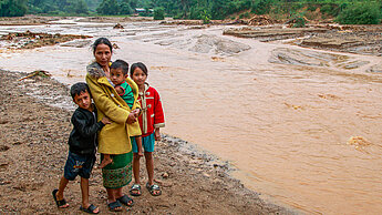 Eine Mutter steht mit ihren drei Kindern an einem schlammigen Ufer eines überschwemmten Gebiets