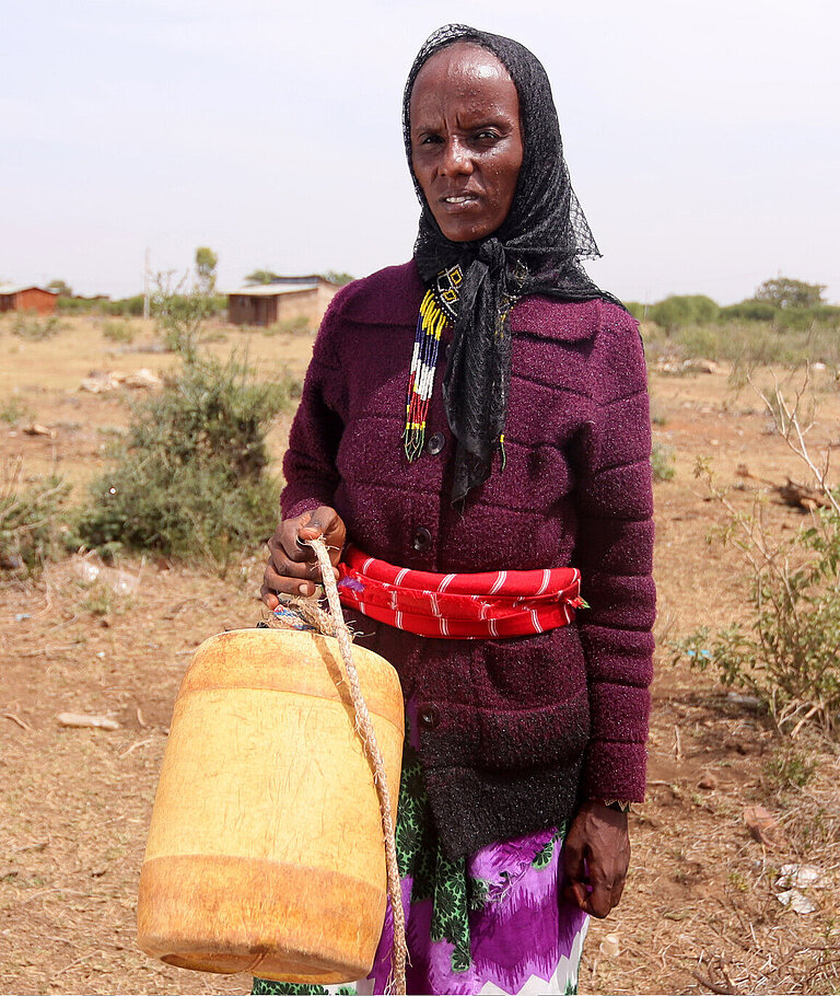 Eine Frau steht auf trockenem Land und hält einen Kanister für Wasser in der Hand