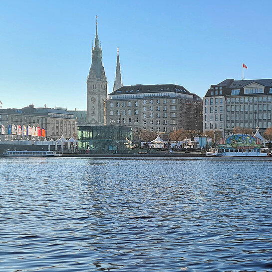 Blick auf die Hamburger Innenstadt mit Rathaus sowie Binnenalster, auf der mehrere Ausflugsschiffe zu sehen sind