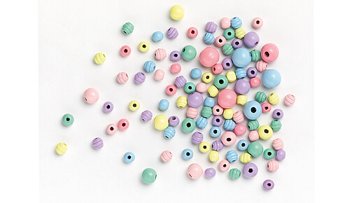 verstreut liegende Holzperlen in hellgelb, mint, hellblau, rosa und flieder in unterschiedlichen Größen.
