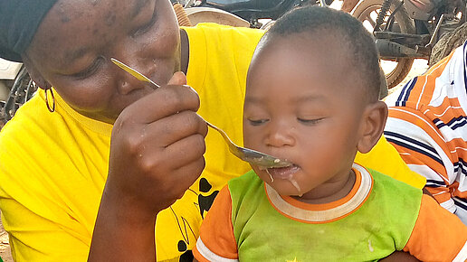 Eine Frau füttert das kleine Kind, das auf ihrem Schoß sitzt.