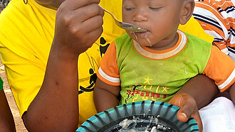 Eine Frau füttert das kleine Kind, das auf ihrem Schoß sitzt.