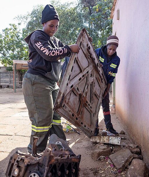 Zwei Frauen mit Overall hieven eine Motorhaube zur Seite