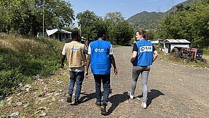 Drei Plan-Mitarbeitende gehen über einen Sandweg in einer ländlichen Region Äthiopien. Sie tragen Westen mit dem Logo von Plan International.