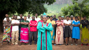 Gemeindeleiterin in traditioneller Kleidung steht selbstbewusst vor ihrer Community in Malawi