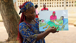 Frau in traditioneller Kleidung zeigt eine Illustration zur Geburtshilfe in Togo – Teil einer Aufklärungskampagne.