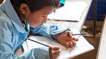 Ein kleiner Junge hält in beiden Händen einen Bleistift und malt nach Zahlen in einem Heft