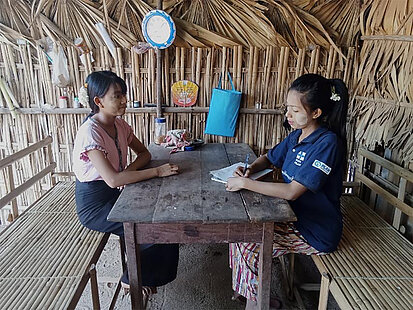 Zwei junge Frauen sprechen in einer Bambushütte miteinander