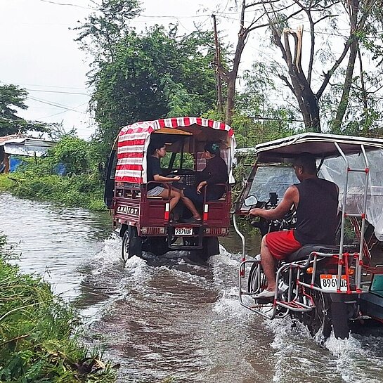 Menschen überqueren zu Fuß und in Tricycles die überfluteten Straßen in der Region MIMAROPA