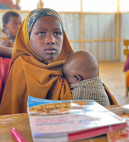Ein somalisches Mädchen sitzt in der Schule und hat seine nur wenige Monate alte Schwester dabei
