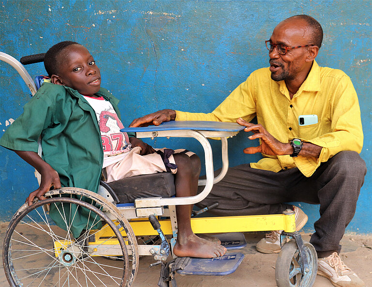 Ein Junge im Rollstuhl, neben ihm kniet ein Mann