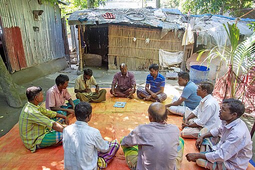 Männer verschiedenen Alters sitzen auf Decken zusammen in einem Kreis unter Bäumen