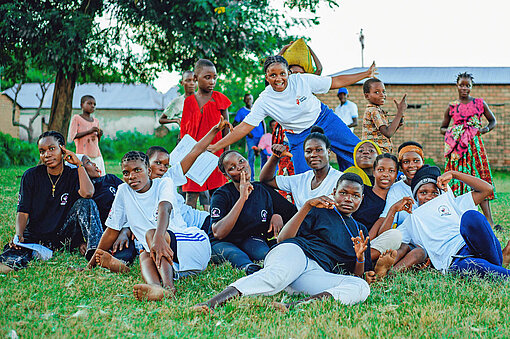 Eine Gruppe Mädchen und Jungen liegt zusammen auf dem Rasen vor einem Haus