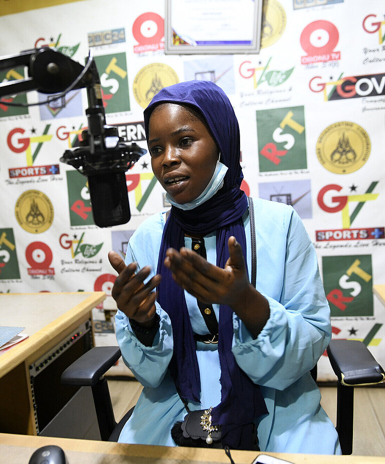 Eine junge Frau sitzt in einem Radiostudio und spricht in ein Mikrofon