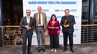 Vier Personen stehen vor einer Wand mit dem Logo von Plan International