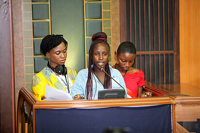 Junge Aktivistinnen präsentieren ihre Forderungen bei einer offiziellen Konferenz zur Stärkung von Mädchenrechten in Senegal Drei junge Frauen sprechen bei einer Veranstaltung in Senegal am Rednerpult über ihre Rechte und Anliegen