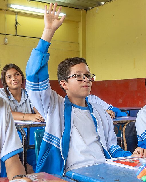 Jesús (14) hatte die Idee für eine Schulspargruppe, die etwas für den Umwelt- und Resscourcenschutz unternimmt Ein Junge mit einem Trainingsanzug sitzt in eine Schulbank und meldet sich