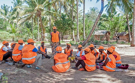 Eine Gruppe Menschen sitzt unter Palmen zusammen
