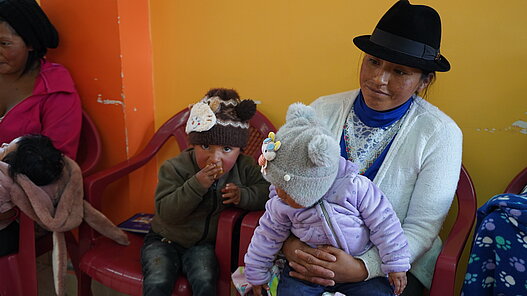 Eine Mutter und ihre zwei kleinen Kinder beim einer Schulung von Plan.