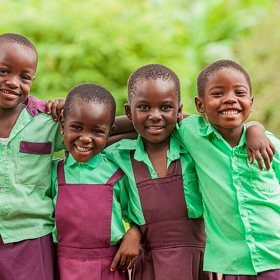 Vier Kinder in Schuluniformen legen sich die Arme um die Schultern