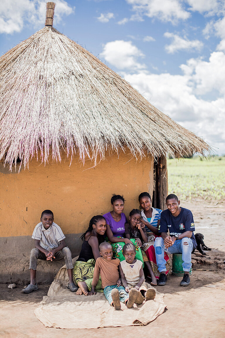Der 23-jährige Junge Boyd sitzt mit seinen Geschwistern vor einem traditionellen Haus in der Zentralprovinz von Sambia