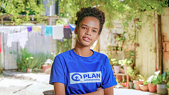 Eine junge Frau steht mit verschränkten Armen und schaut ernst in die Kamera