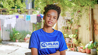 Eine junge Frau steht mit verschränkten Armen und schaut ernst in die Kamera