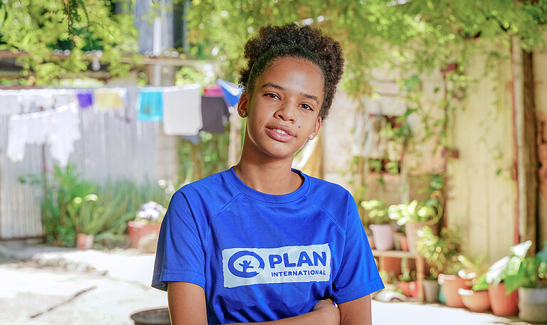 Eine junge Frau steht mit verschränkten Armen und schaut ernst in die Kamera