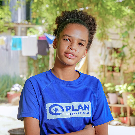 Eine junge Frau steht mit verschränkten Armen und schaut ernst in die Kamera