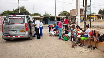 Ein kleiner Bus steht auf einer Straße, daneben stehen viele Menschen