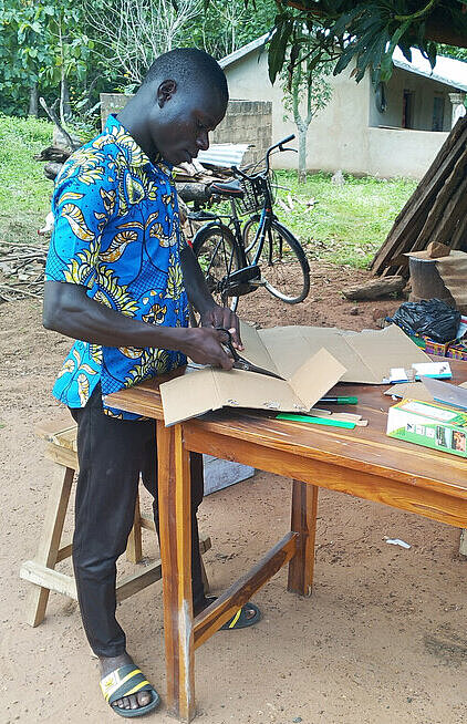 Junger Mann schneidet draußen an einem Tisch Pappe zurecht