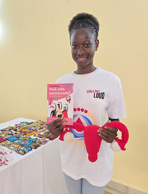 Carla präsentiert verschiedene Materialien bei einer Veranstaltung zum Tag der Menstruationsgesundheit Carla steht bei einer Aufklärungsveranstaltung zum Menstruationsgesundheitstag und zeigt Informationsmaterialien zur Menstruationshygiene