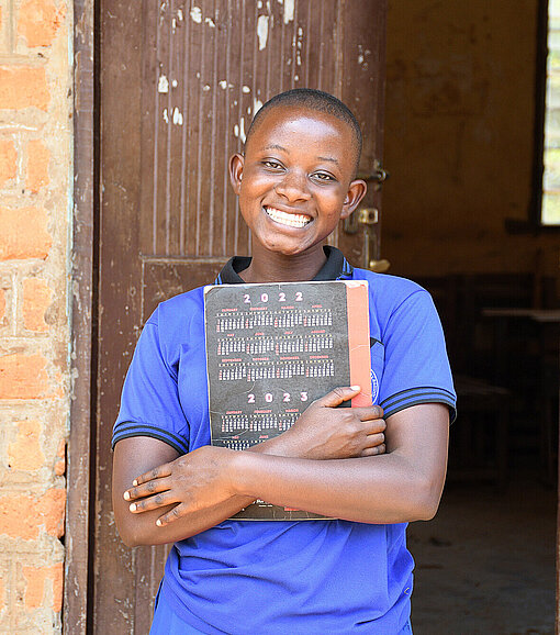 Ein Mädchen steht in einer Tür und hält ein Schulbuch fest vor die Brust