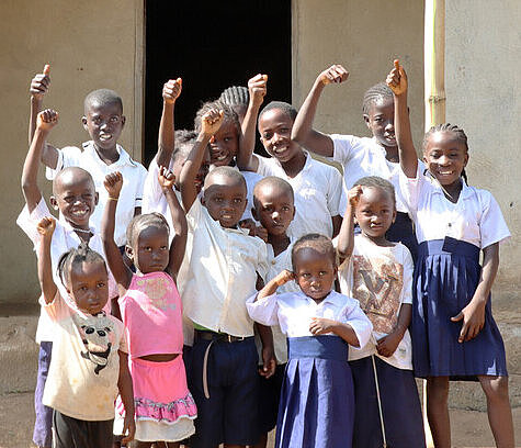 Kinder aus Liberia stehen vor ihrer neuen Schule in Lofa und strecken ihre Hände hoch