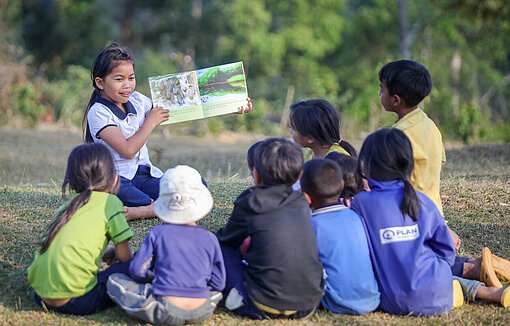 Mädchen zeigt einer Gruppe von Kindern im Freien Informationen zum Klimawandel.