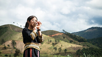 Ein Mädchen aus Vietnam steht draußen und hält beide Hände vor den Mund, als würde es etwas rufen