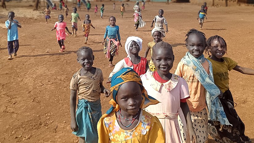 Geflüchtete Kinder in Ura, die mit Freude auf die Betrachter*in zugelaufen kommen.