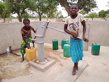 Zwei Kinder holen Trinkwasser an einer Pumpe