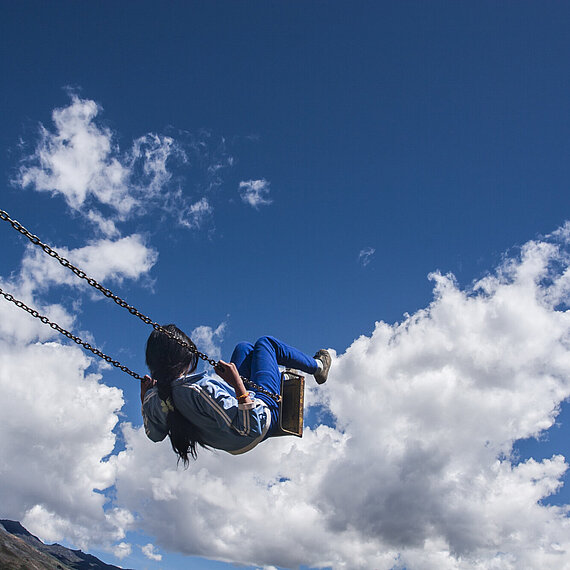 Symbolbild für Perspektiven schaffen durch Immobilienvererbung Kind auf einer Schaukel vor blauem Himmel – Symbolbild für Freiheit, Sicherheit und Zukunft