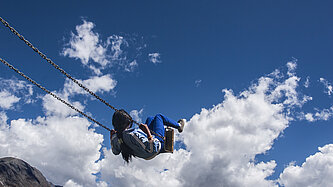 Kind auf einer Schaukel vor blauem Himmel – Symbolbild für Freiheit, Sicherheit und Zukunft