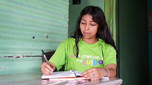 Mädchen in El Salvador lernt und macht Hausaufgaben für die Schule Mädchen in El Salvador sitzt am Tisch und macht Hausaufgaben in einem Heft