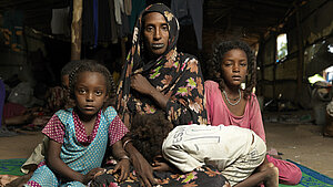 Geflüchtete Familie aus dem Sudan mit Mutter und Kindern, die in einer provisorischen Unterkunft sitzen.