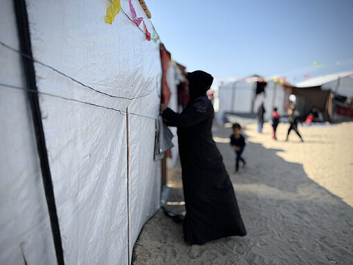 Mutter aus Gaza steht in schwarz gekleidet an einer Zeltwand 